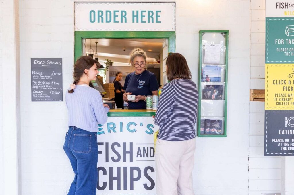 Two women ordering food with another woman at an 'Order Here' point at Eric's Fish and Chips