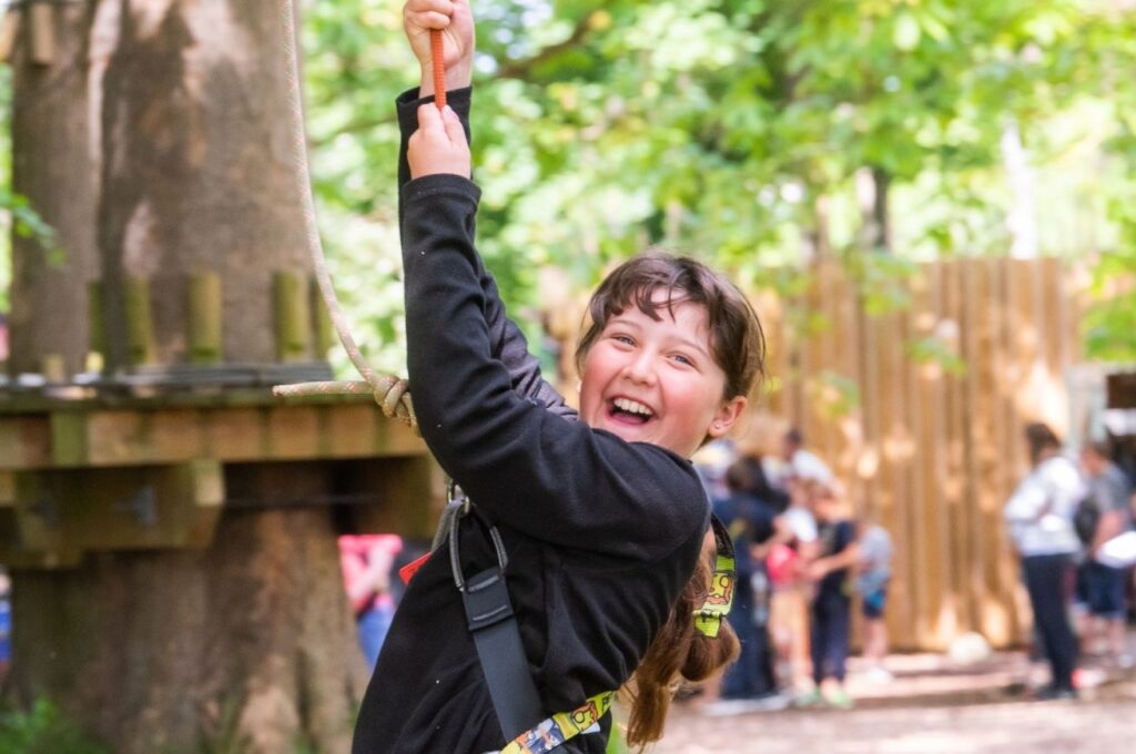 A child grinning on Holkham ropes course with a harness on