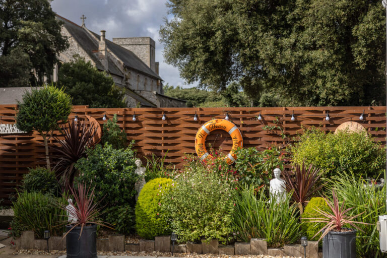 Flower bed backed with a fence with a life bouy hanging on it as decoration