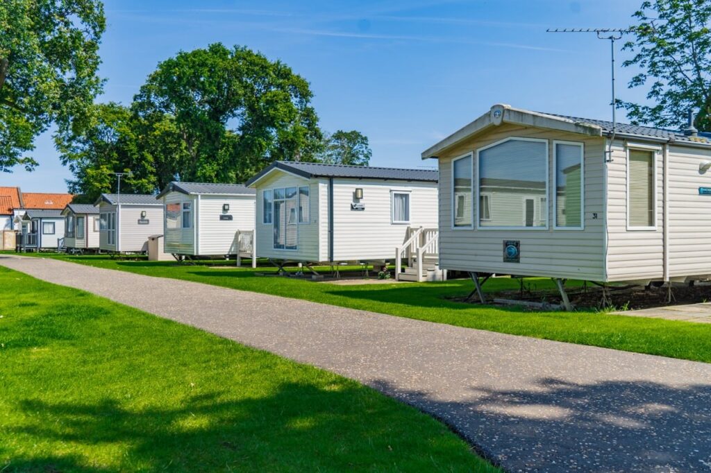 A row of spaced out static caravans on grass next to a concrete path